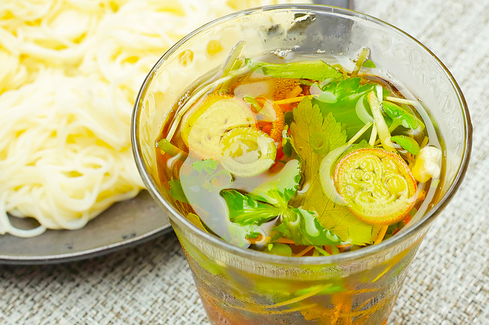 冷麺と一緒に提供される、薬味やハーブが入った透明なスープ入りのグラス。