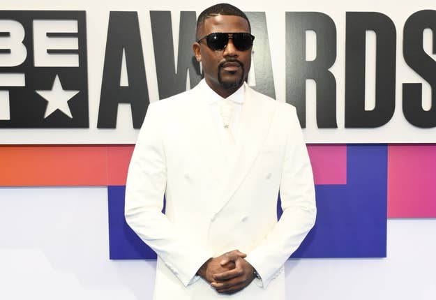 Ray J in a white suit with black sunglasses at the BET Awards, posing in front of a sign with "BET AWARDS" text