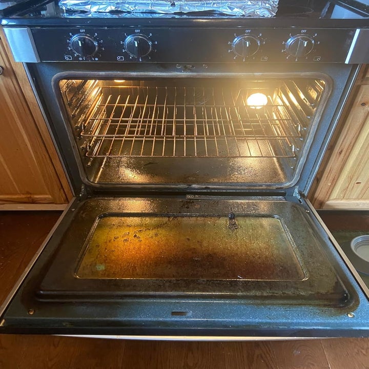 Open oven in a kitchen with wooden cabinets, showing a dirty bottom and oven racks