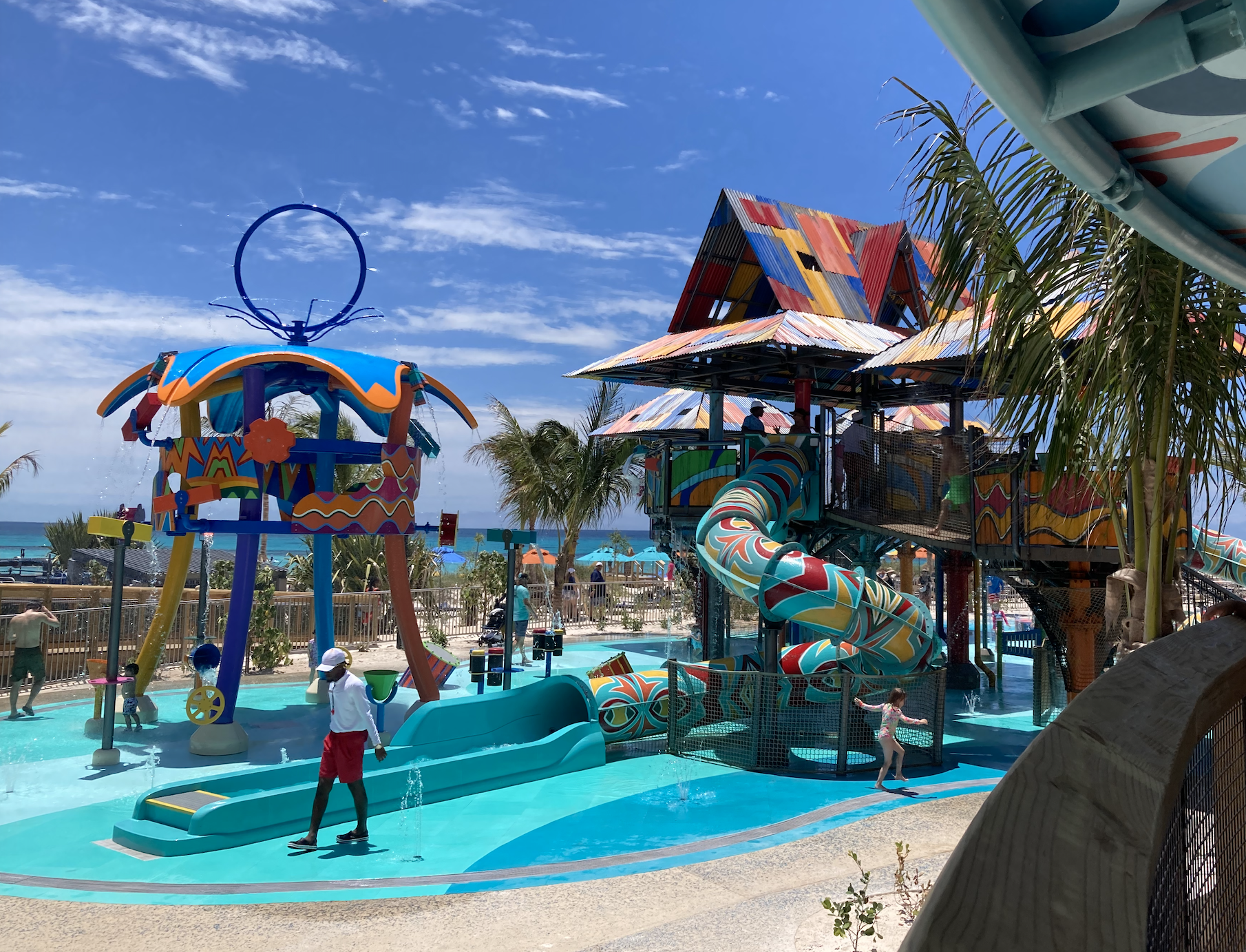 People enjoying a vibrant water play area with slides and colorful structures at a beachside waterpark on a sunny day