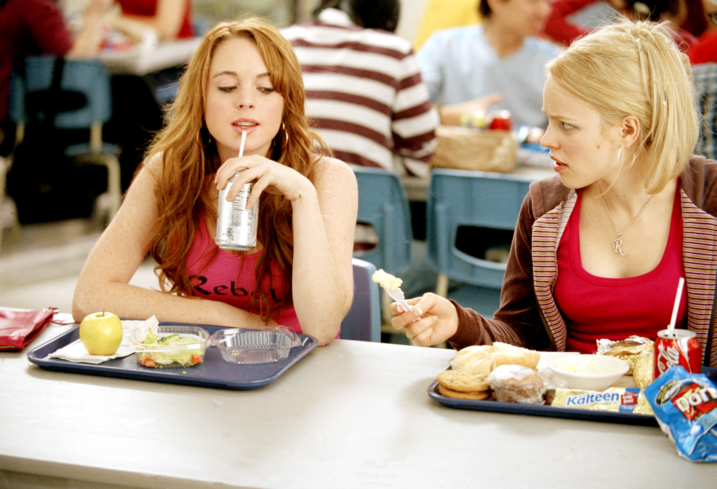 Lindsay Lohan and Rachel McAdams in a school cafeteria scene. Lindsay sips a soda. Rachel looks at her with a skeptical expression