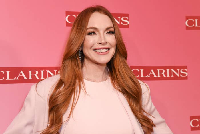 Lindsay Lohan smiling astatine  a Clarins event, with long, wavy hairsbreadth  and dressed successful  a simple, elegant outfit