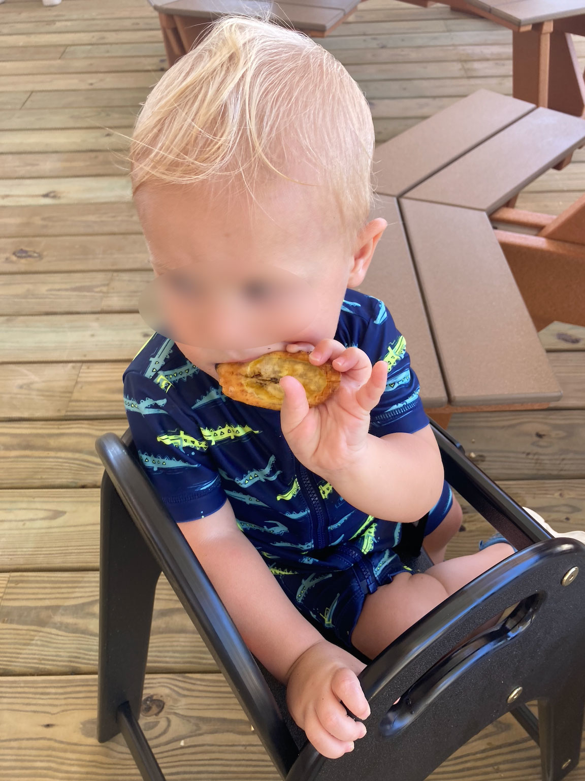 A young child with light hair, seated in a high chair, eating a snack
