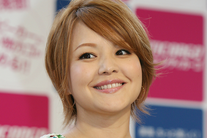 背景に広告用のカラーのスクリーンがあるイベントで、花柄のブラウスを着た女性が笑顔を見せている。