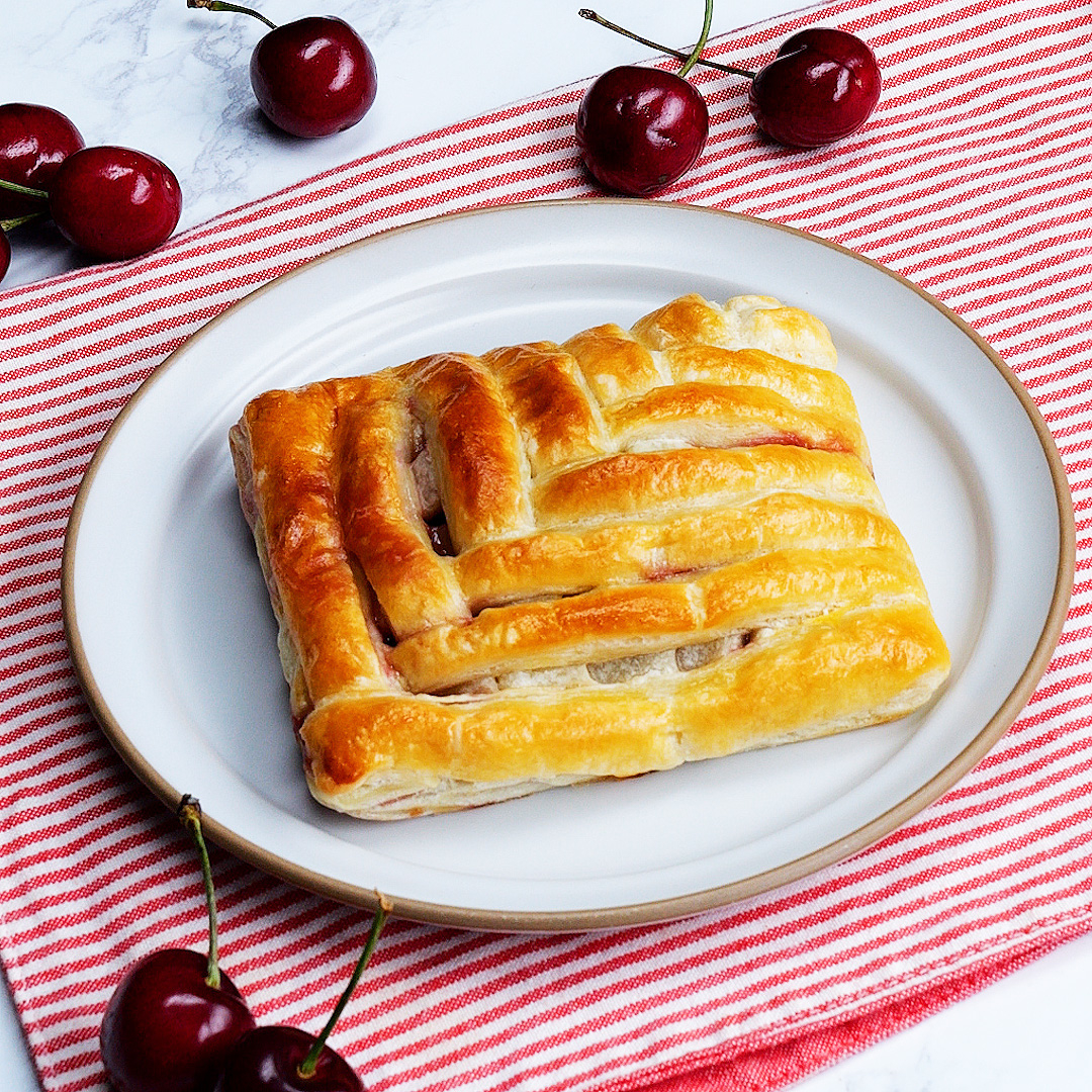 皿の上にあるチェリーパイ。背景には赤と白のストライプの布とチェリーが並んでいる。