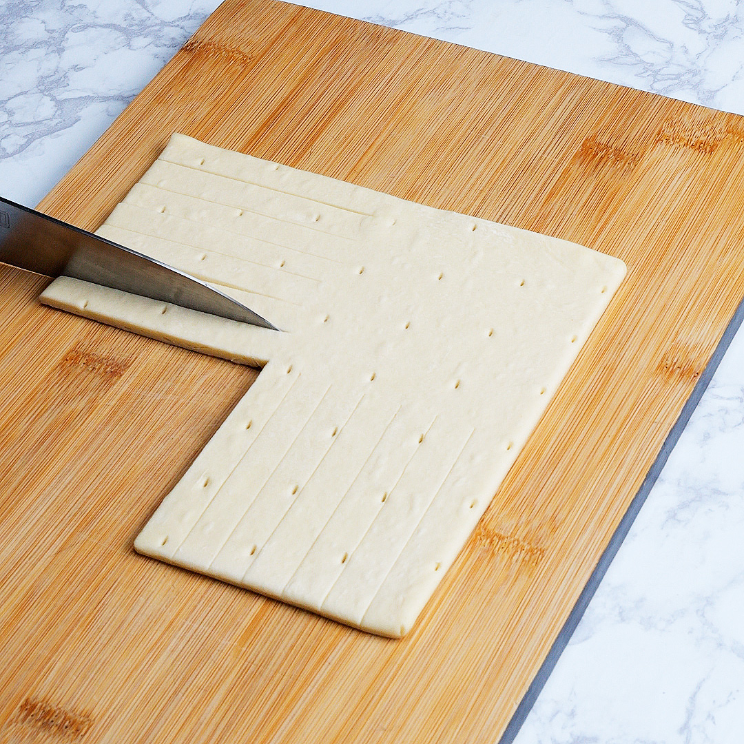 包丁で木製のカッティングボード上にある生地をカットしている場面。