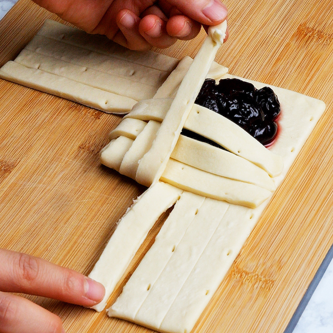 木製のまな板の上でジャムをパイ生地で包む手元の写真。