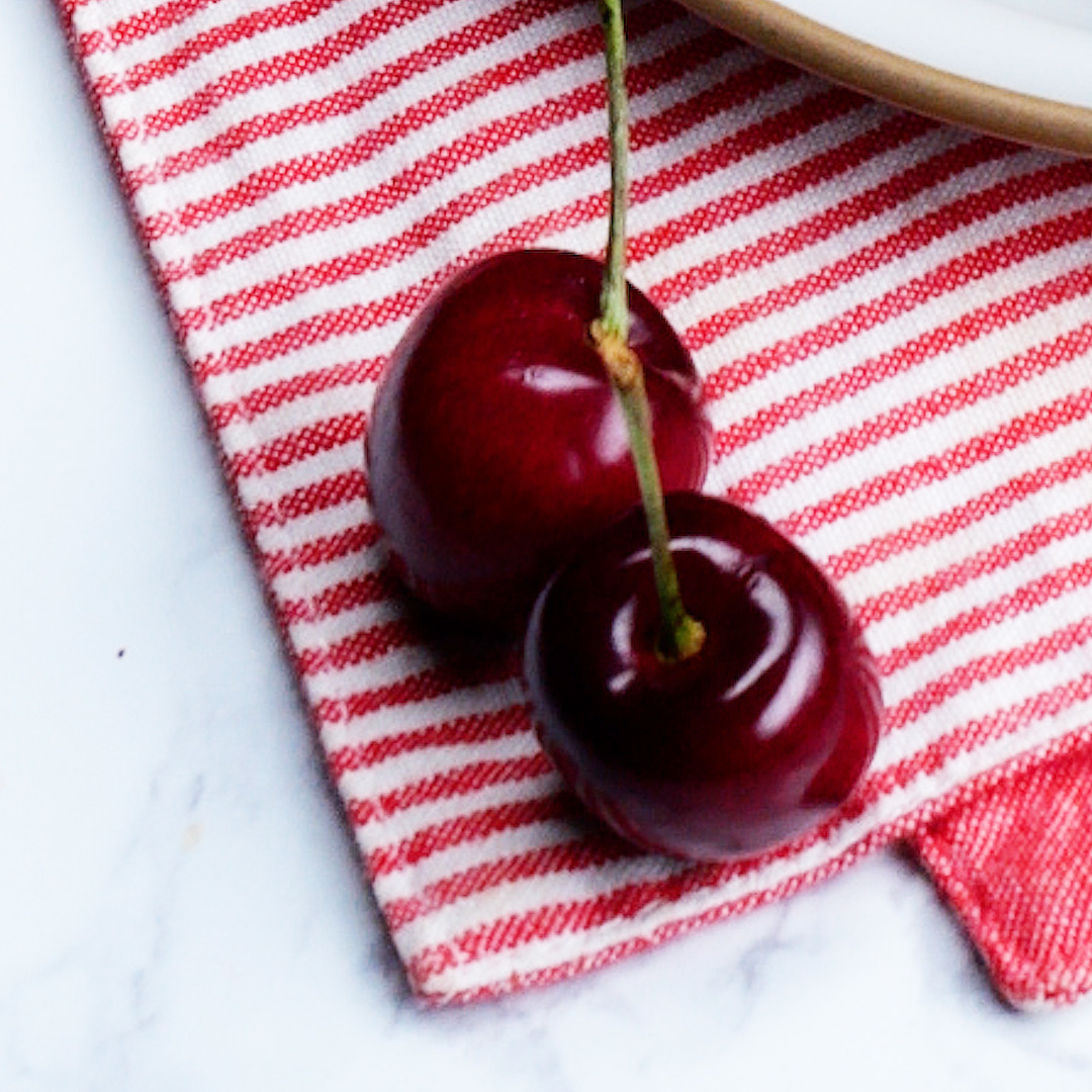 白いプレートと赤いしま模様の布の上に置かれた2つのさくらんぼ。