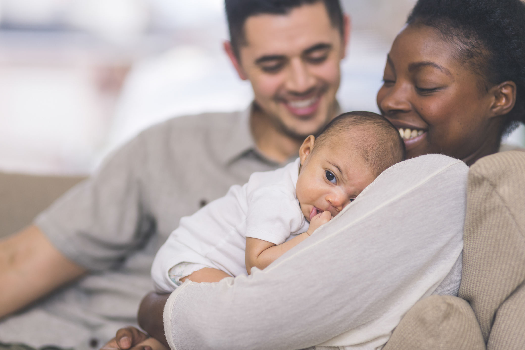 A happy couple, names unknown, smiling at their newborn baby who is resting on the mother's chest