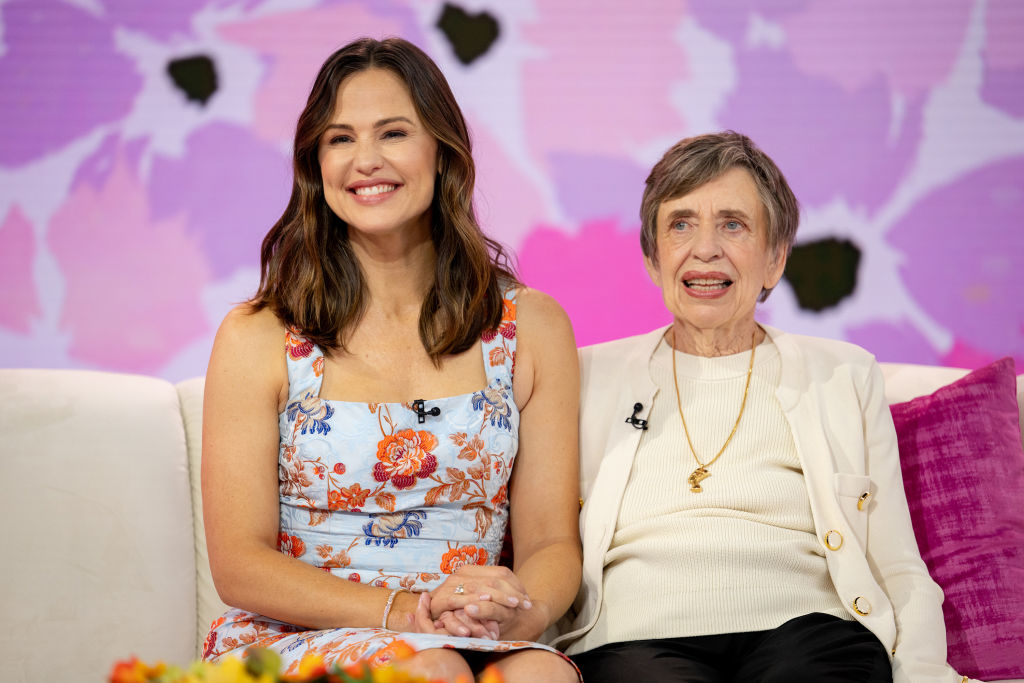 Jennifer Garner and Patricia Garner sit on a couch. Jennifer wears a floral dress, and Dr. Edith Eger wears a white blazer over a light sweater
