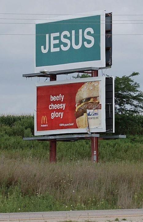 Billboard with two signs: one reading "JESUS" in large text and another below showing a McDonald's burger with the text "beefy cheesy glory."