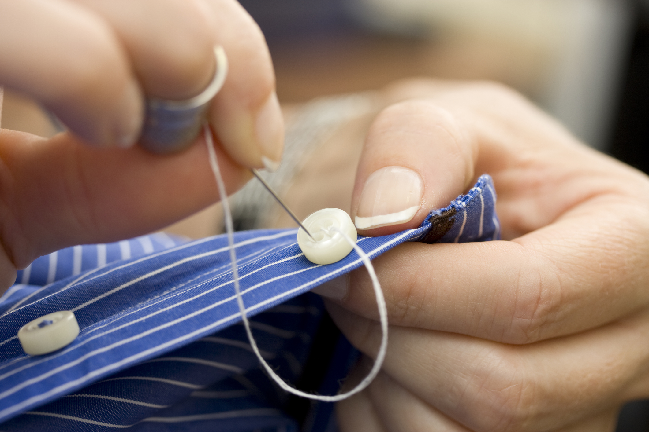 Close-up of someone sewing a button onto a shirt