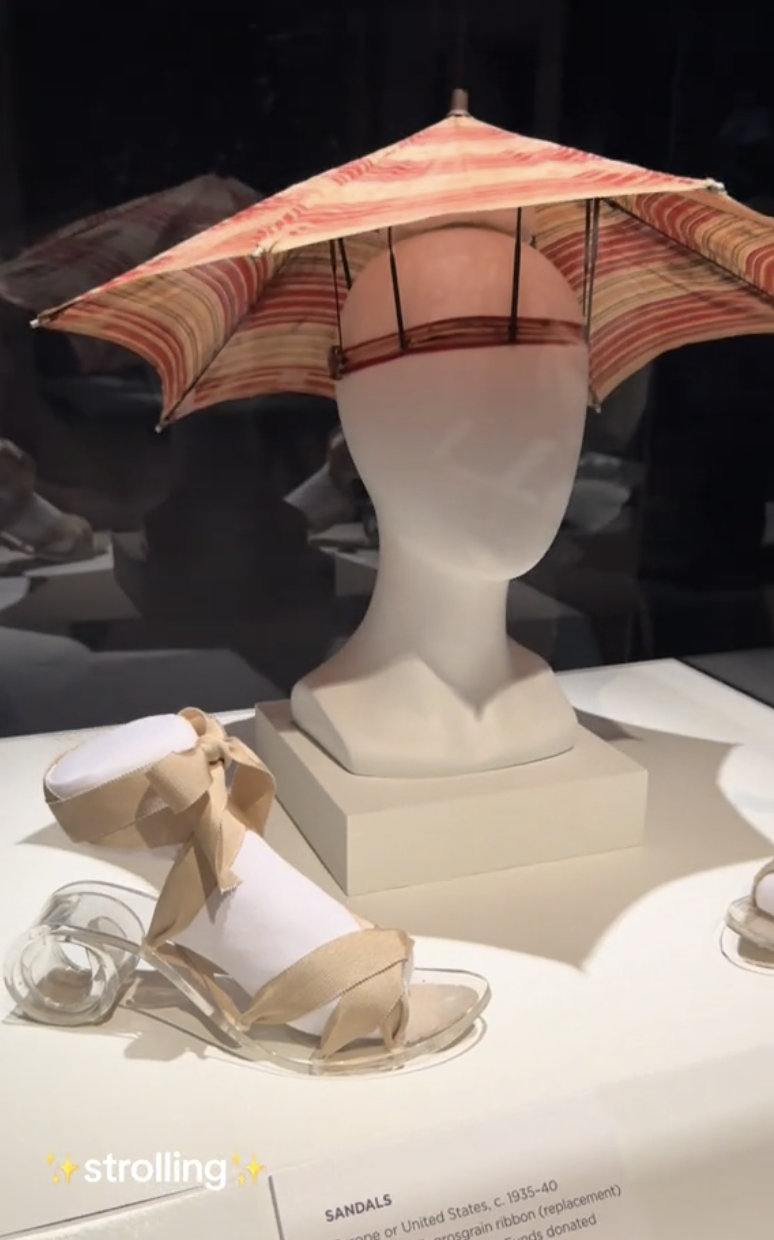 Display of an umbrella hat on a mannequin head, with ribbon-tied sandals nearby. Text overlay reads: &quot;✨strolling✨.&quot;