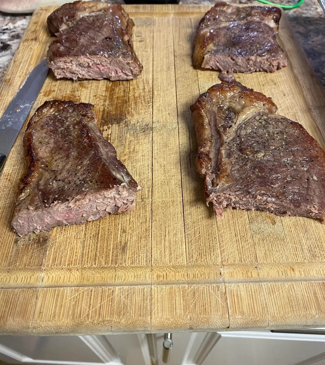 Cooked, seasoned steak pieces on a wooden cutting board, next to a knife