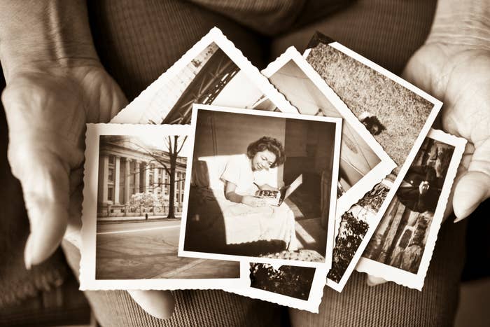 A person holds several black-and-white photographs in their hands, featuring various scenes and a woman smiling while looking at a book