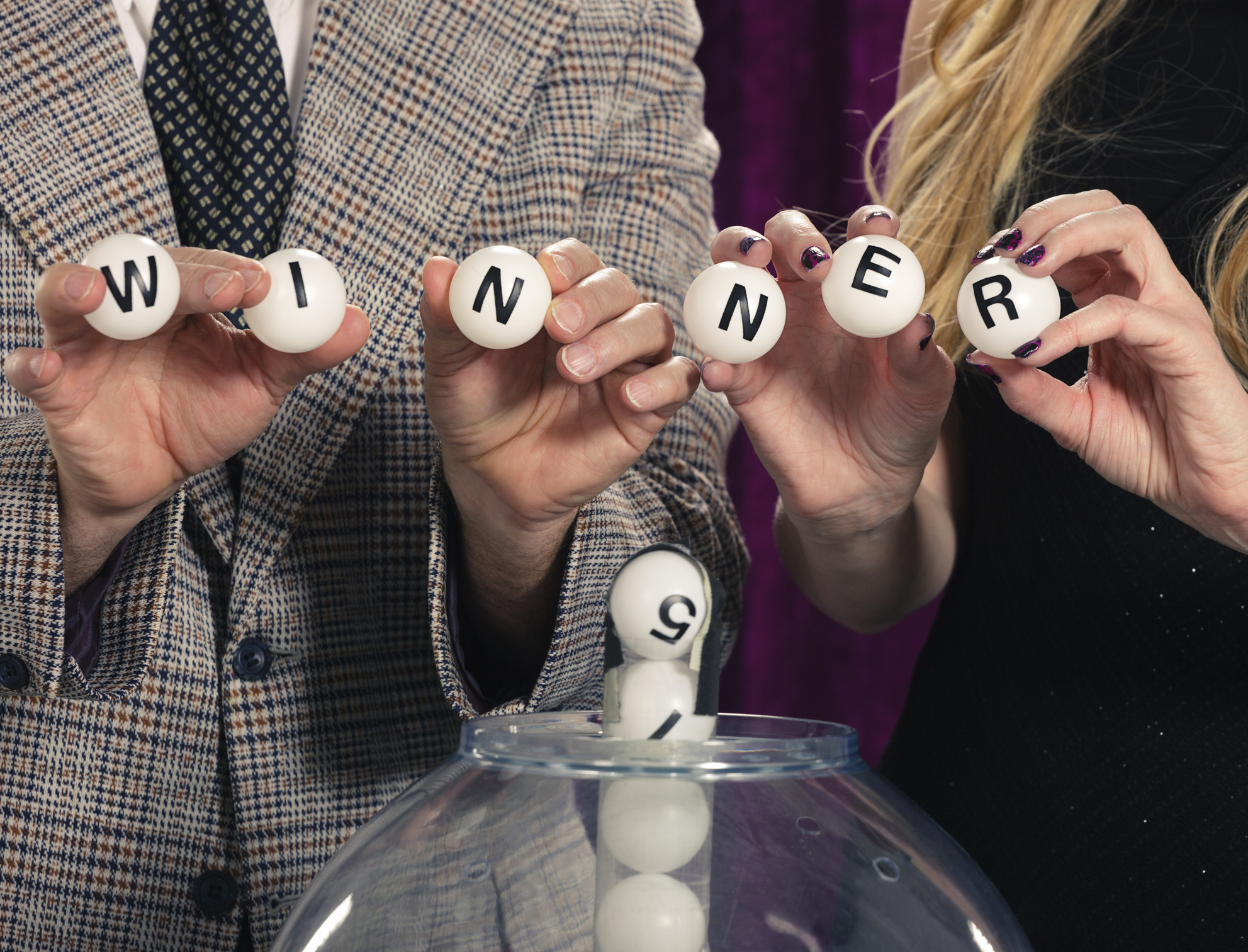 Close-up of three people drawing lottery balls, spelling out &quot;WINNER.&quot;