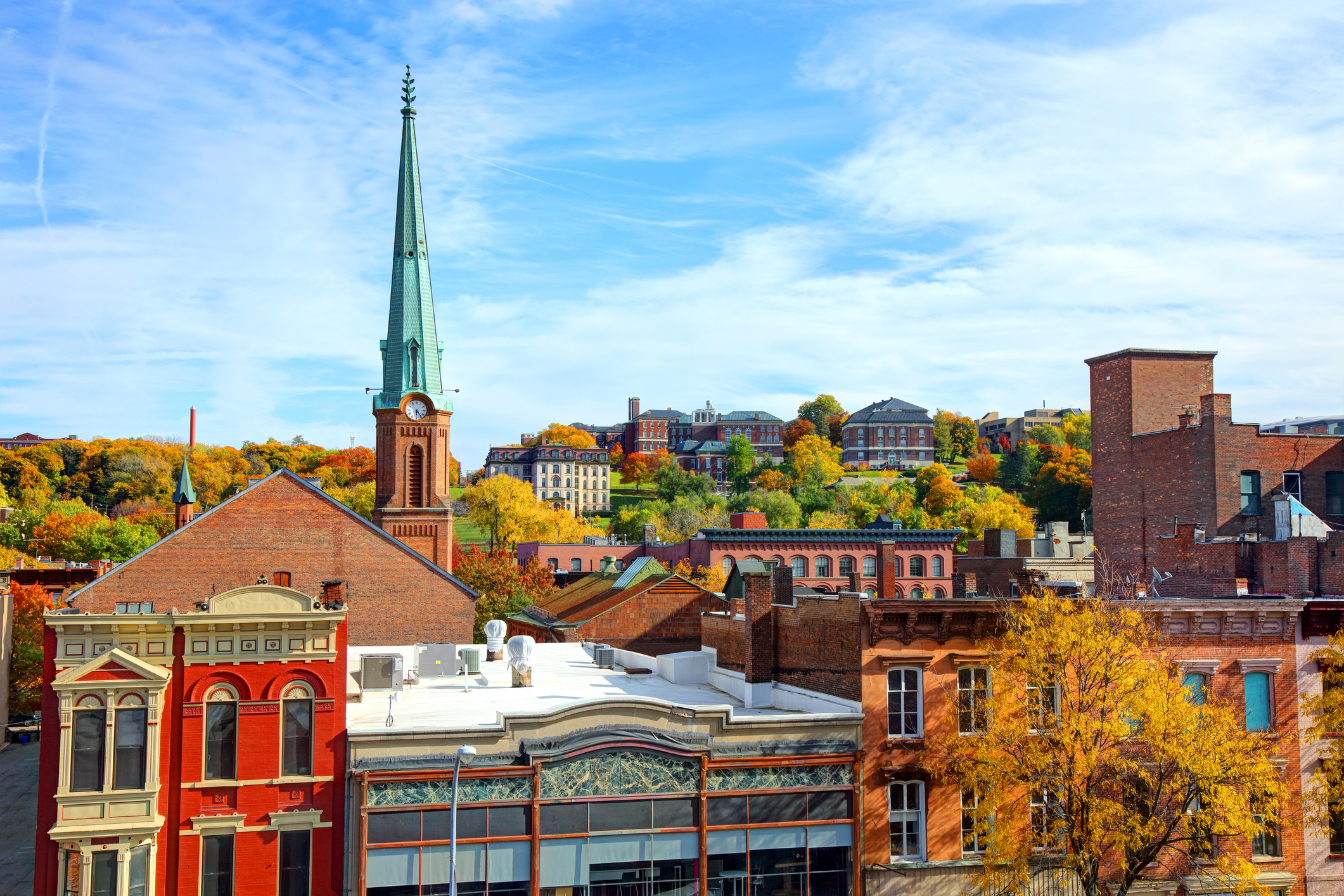 Scenic view of downtown Saratoga Springs, New York, featuring historic buildings and a church steeple against a backdrop of autumn foliage
