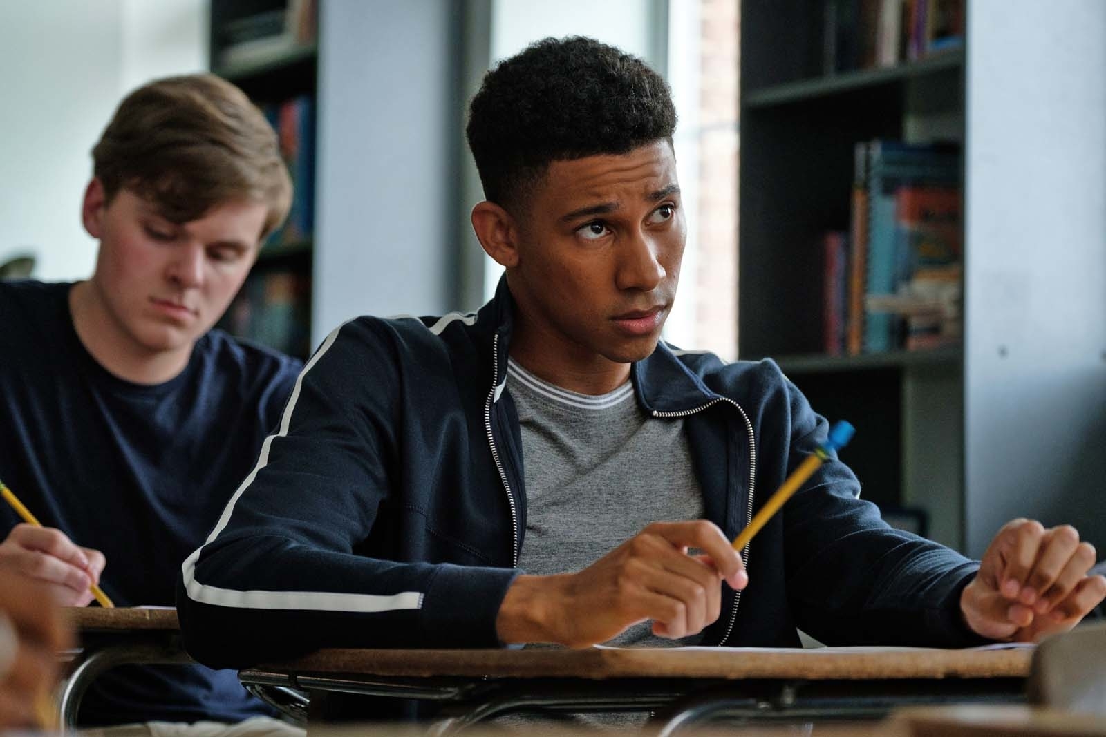 Jabari Banks intently listens during a classroom scene while holding a pencil. Another student, focused on writing, sits behind him