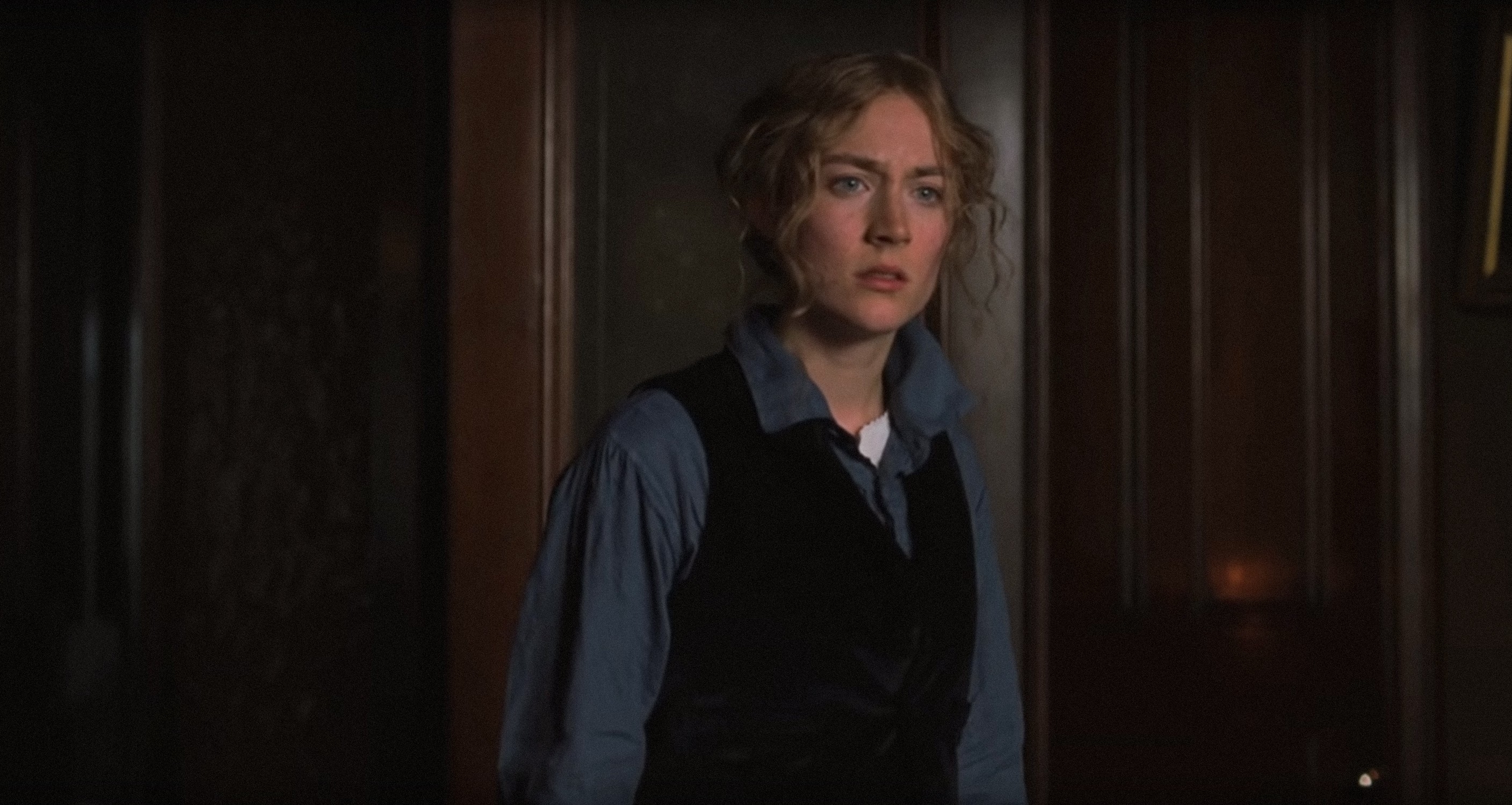 Saoirse Ronan in period clothing, wearing a blue button-up shirt with a black velvet vest, in a scene from a movie