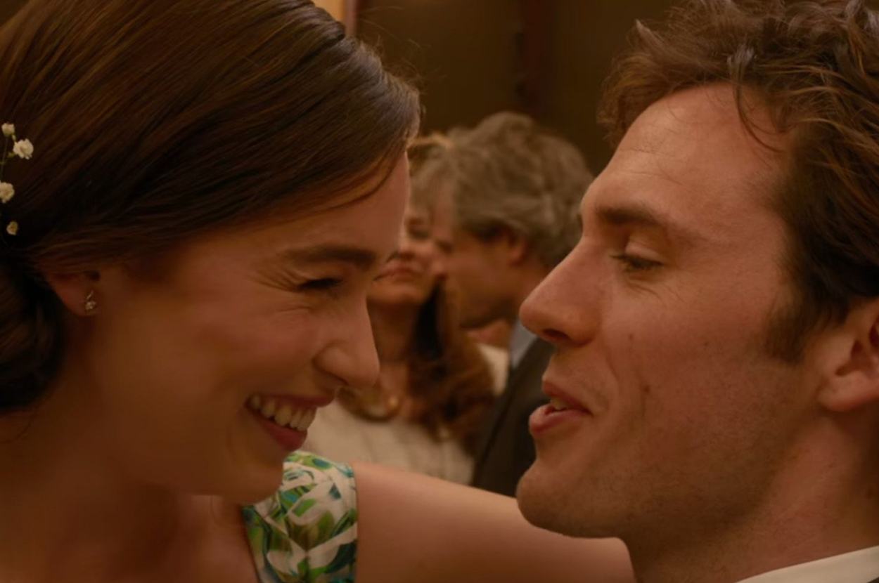 Emilia Clarke and Sam Claflin smile and lean in close to each other at a social event, with people conversing in the background