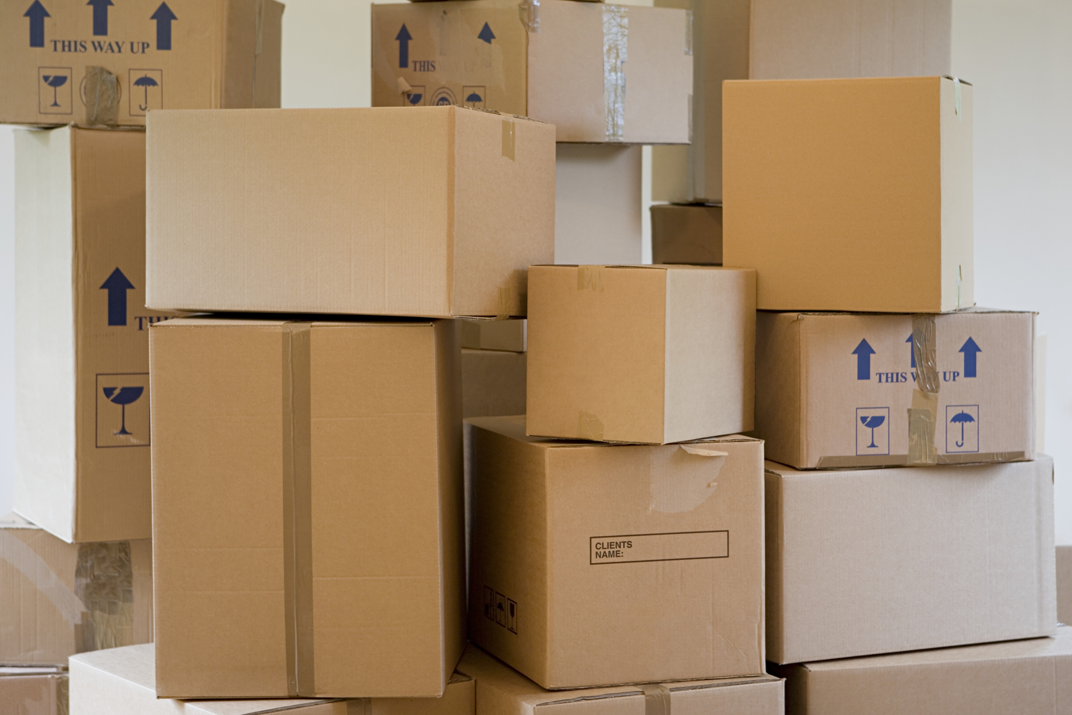 Stack of labeled and unlabeled moving boxes in various sizes, some with &quot;This Way Up&quot; and fragile item symbols, indicating a packing or moving scene
