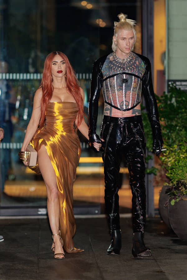 Megan Fox in a gold dress with a high slit and Machine Gun Kelly in a futuristic black and silver outfit walk hand-in-hand