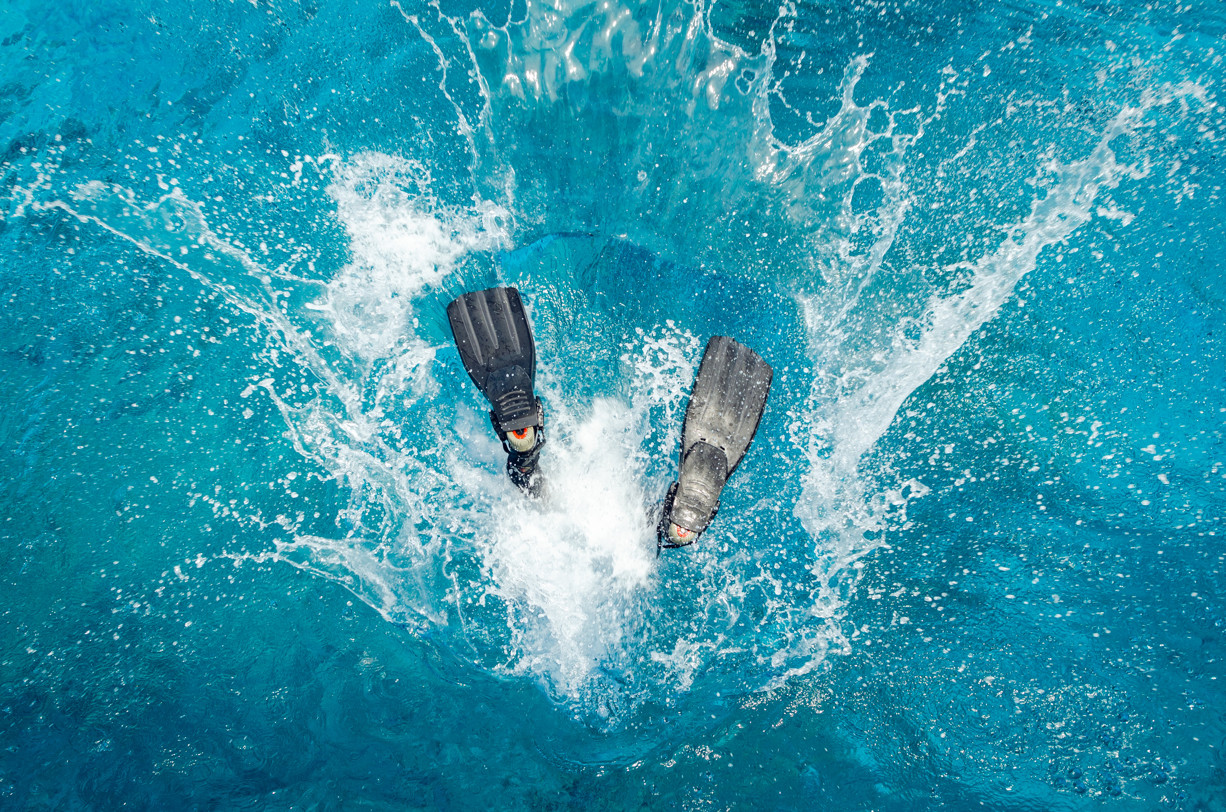 A diver's fins are visible as they enter the water and splash