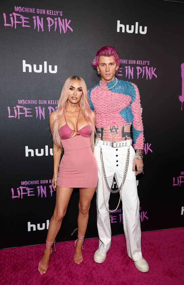 Megan Fox and Machine Gun Kelly on the red carpet at the &quot;Life in Pink&quot; premiere. Megan wears a fitted pink dress, while Machine Gun Kelly wears a pink and blue sweater with white pants