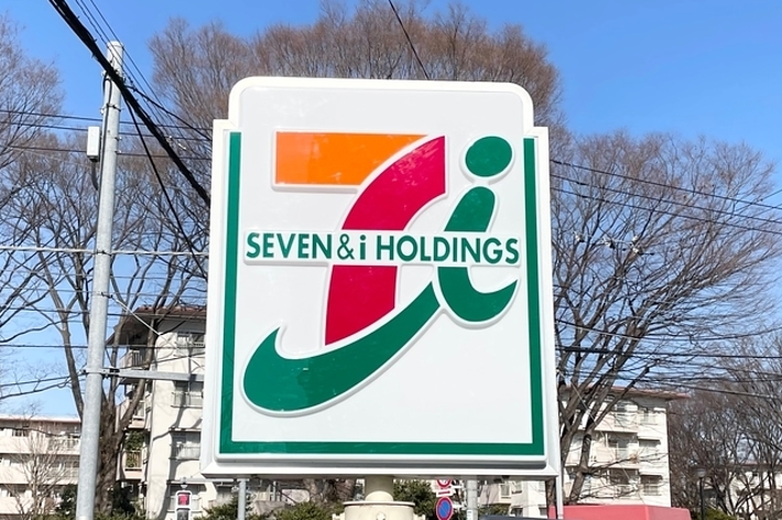 セブン&アイ・ホールディングスの看板と、たばこや酒、ATMの案内が見える。背景には建物と木々が写っている。