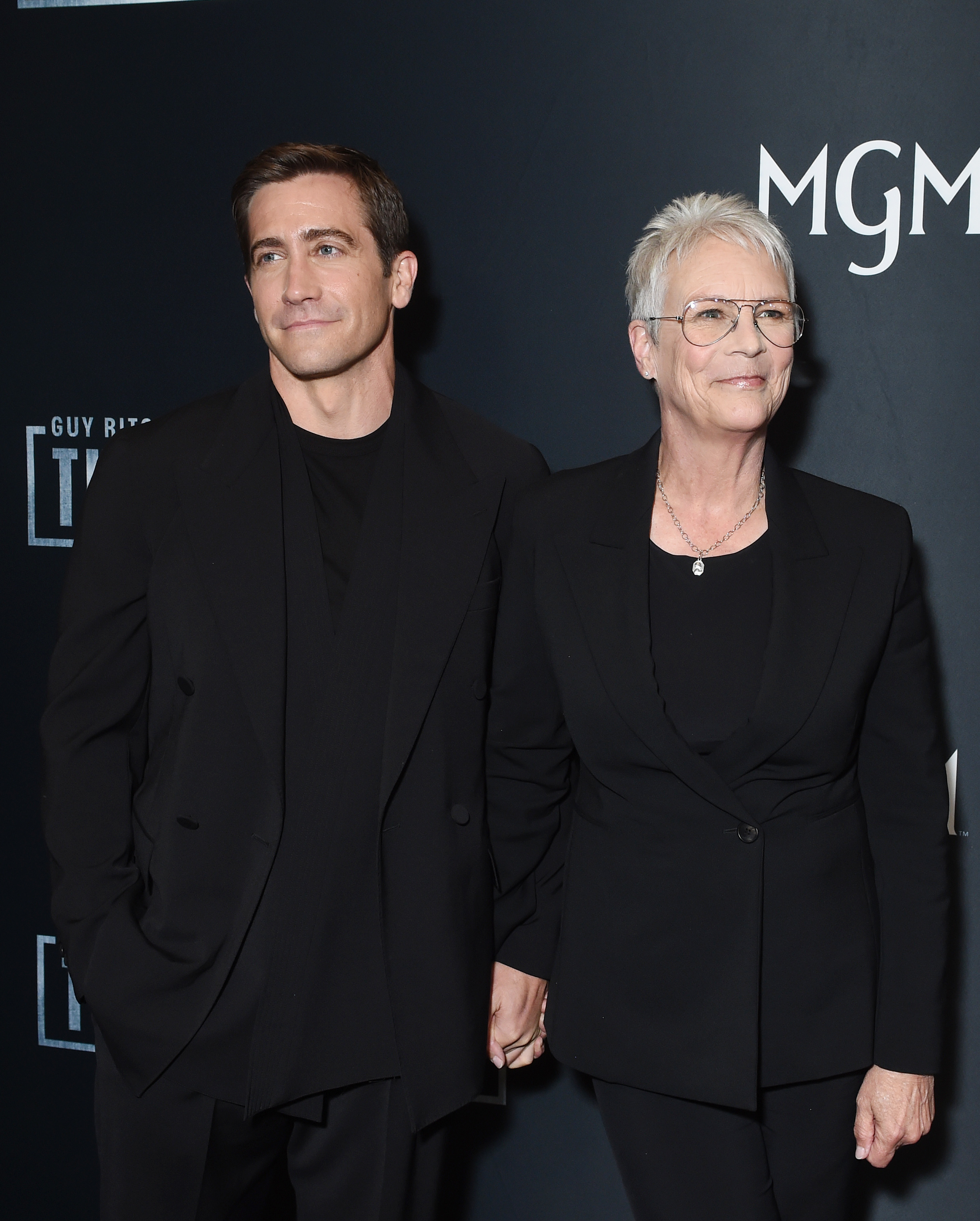 Jake Gyllenhaal and Jamie Lee Curtis pose on the red carpet, both wearing black tailored suits