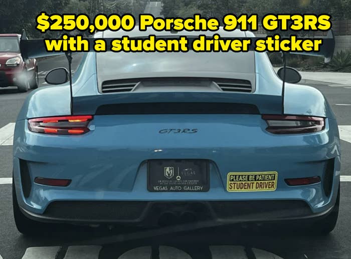 The image shows the rear of a sports car with a spoiler. The license plate frame says "Vegas Auto Gallery," and a bumper sticker reads, "Please be patient, student driver."