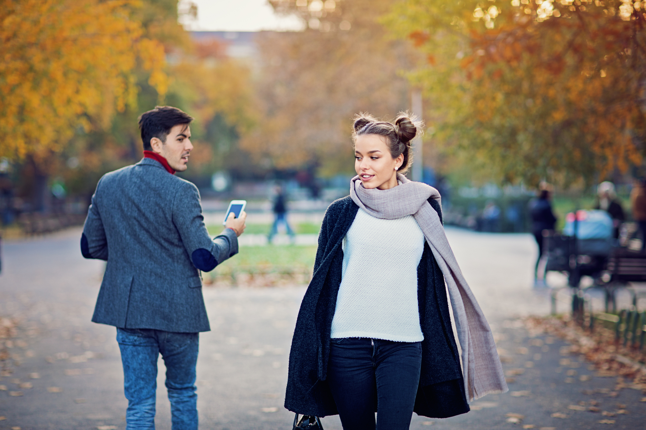 A man looks slightly backwards at a woman he finds attractive as they pass by each other in a park.
