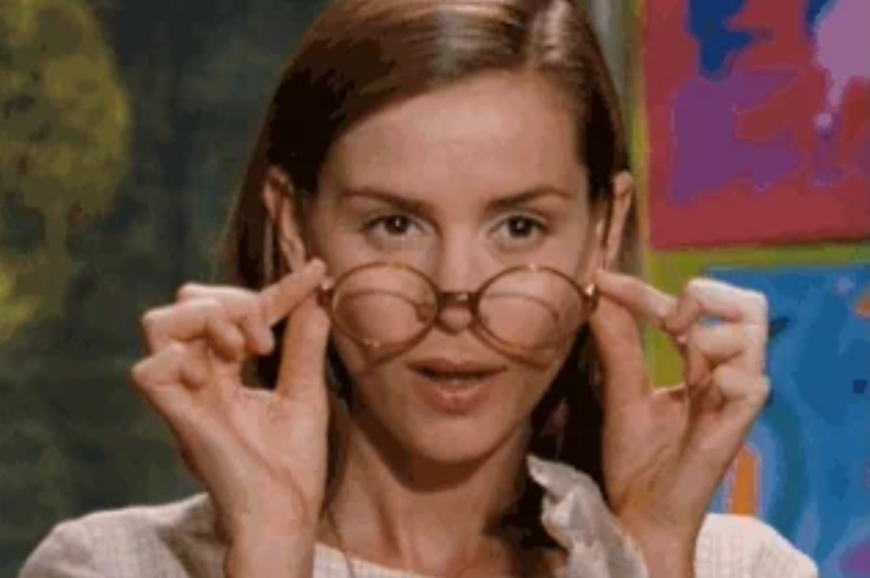 A person adjusts their glasses while looking directly at the camera in a close-up shot