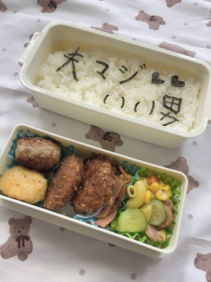 弁当の白ご飯の上に「大マジいい男」と書かれており、下段にはハンバーグ、唐揚げ、野菜などが並んでいます。