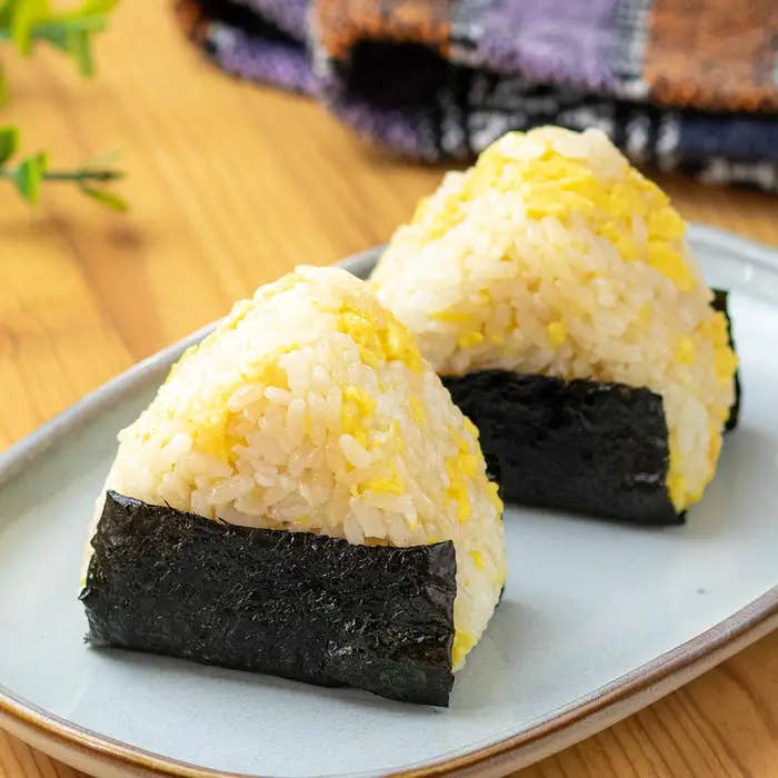 白い皿に盛られた2つののり付きおにぎりの画像。後ろには色とりどりの布地が見える。