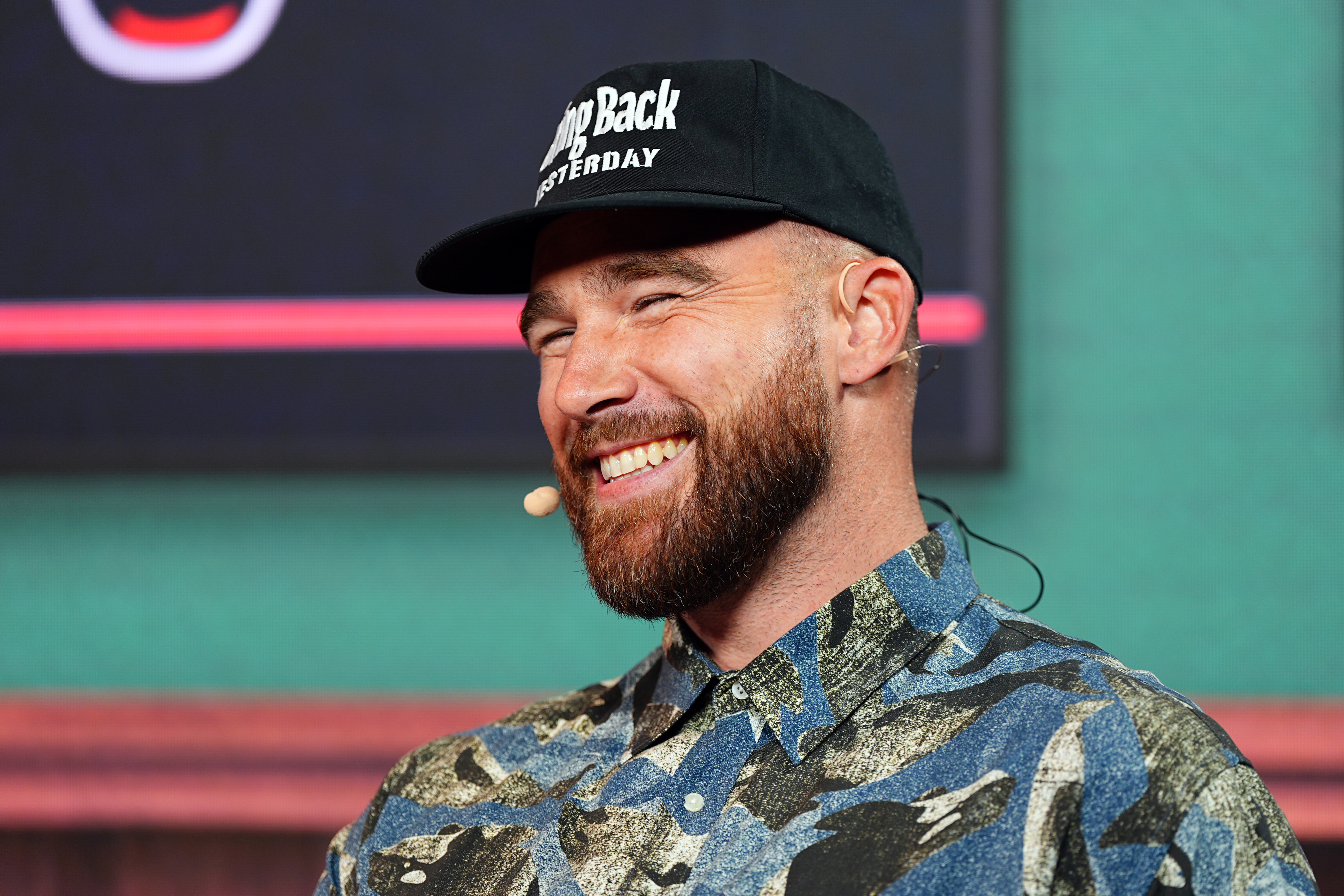 Sean Evans smiling, wearing a patterned button-up shirt and a baseball cap with the text "Step Back Yesterday."