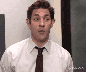 John Krasinski wears a white shirt and tie, making a surprised expression in an office setting