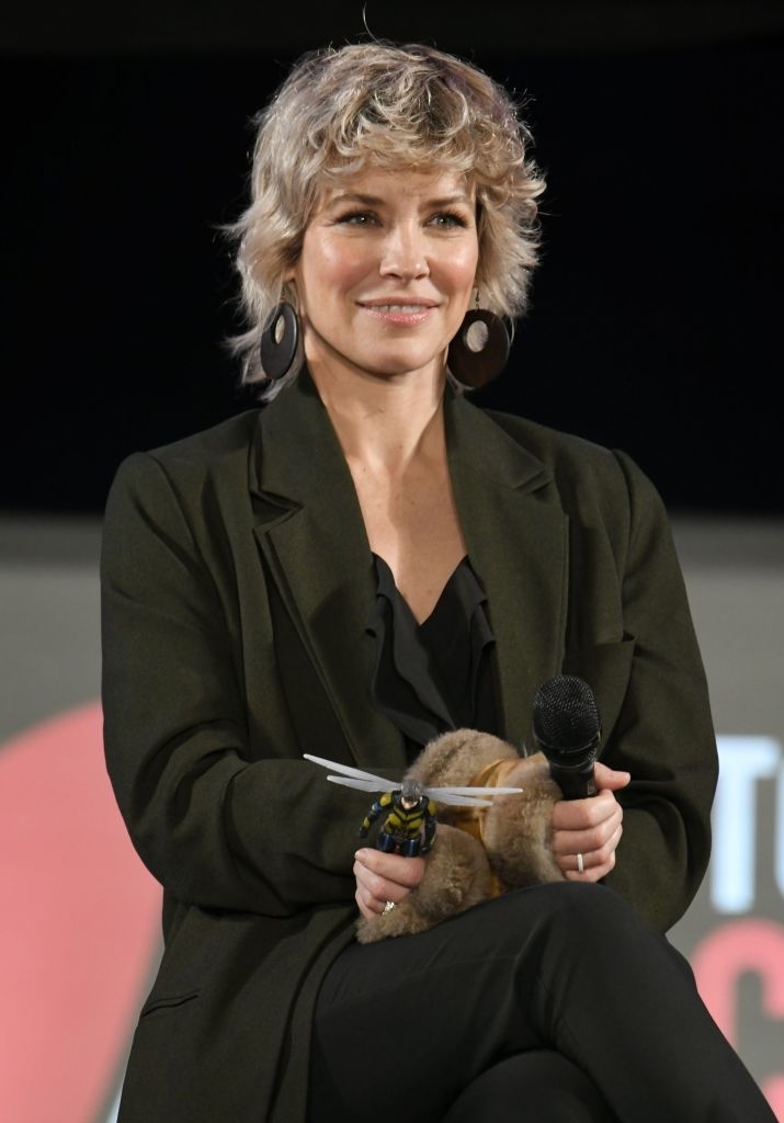 Evangeline with short hair and large earrings, wearing a blazer and holding a microphone on stage