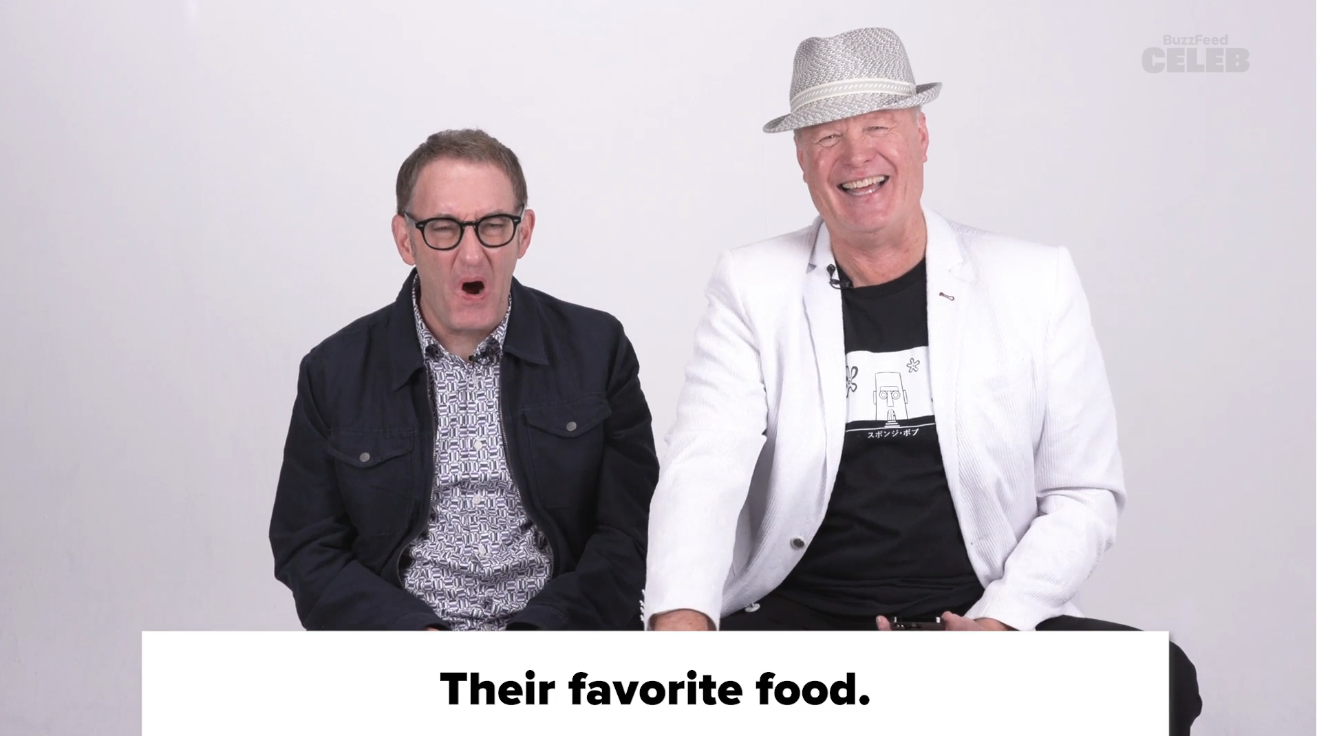 Paul Reubens in a dark jacket and Mark Boone Junior in a white jacket and fedora, sitting next to each other, above the text "Their favorite food."