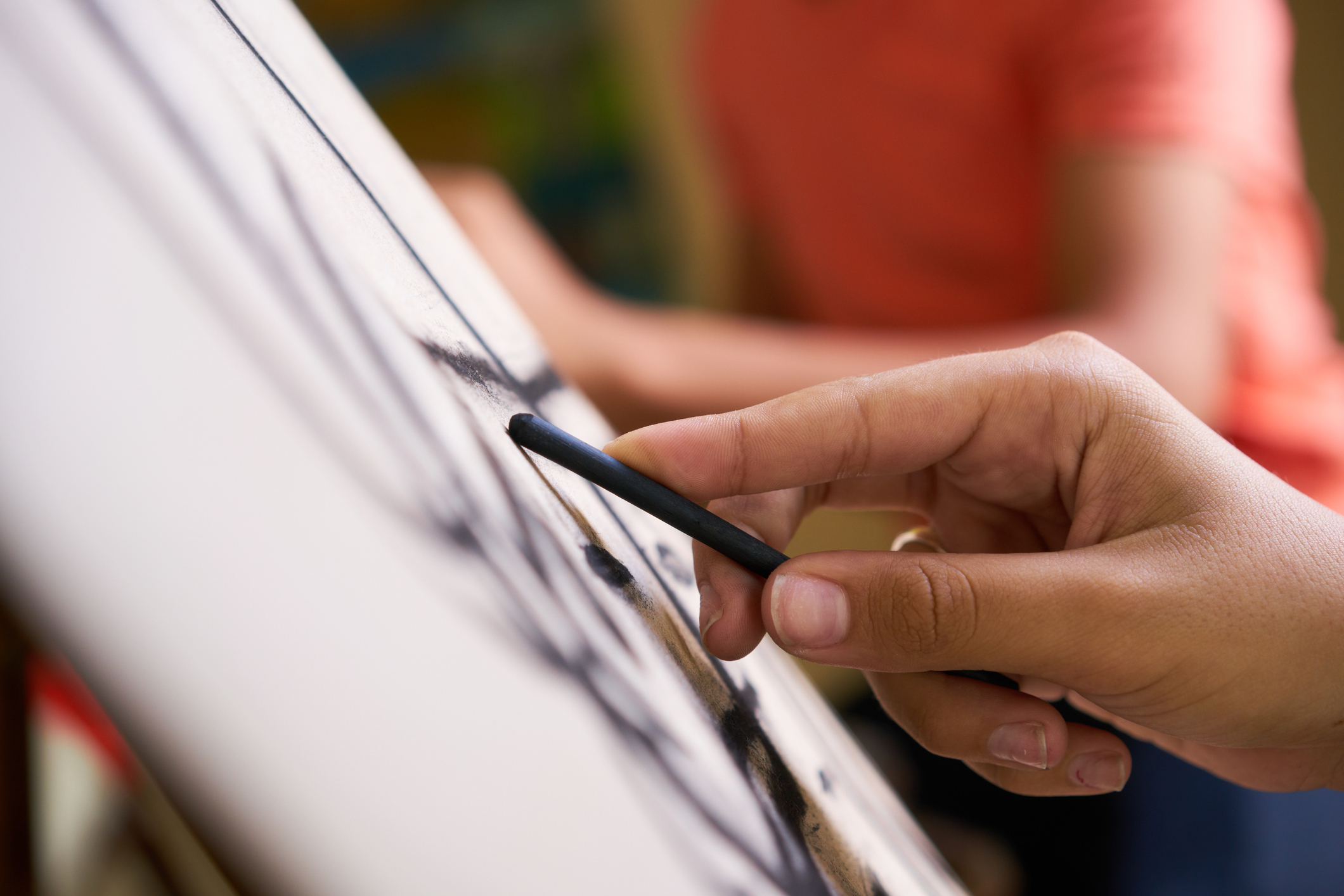Close-up of a person's hand drawing on a canvas with a charcoal stick