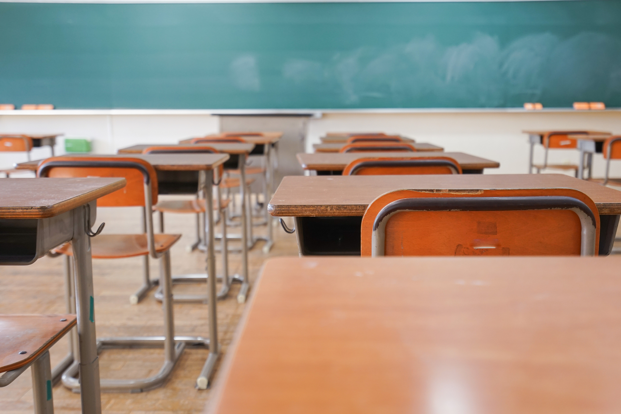 Rows of empty classroom desks and chairs facing a chalkboard in a vacant classroom