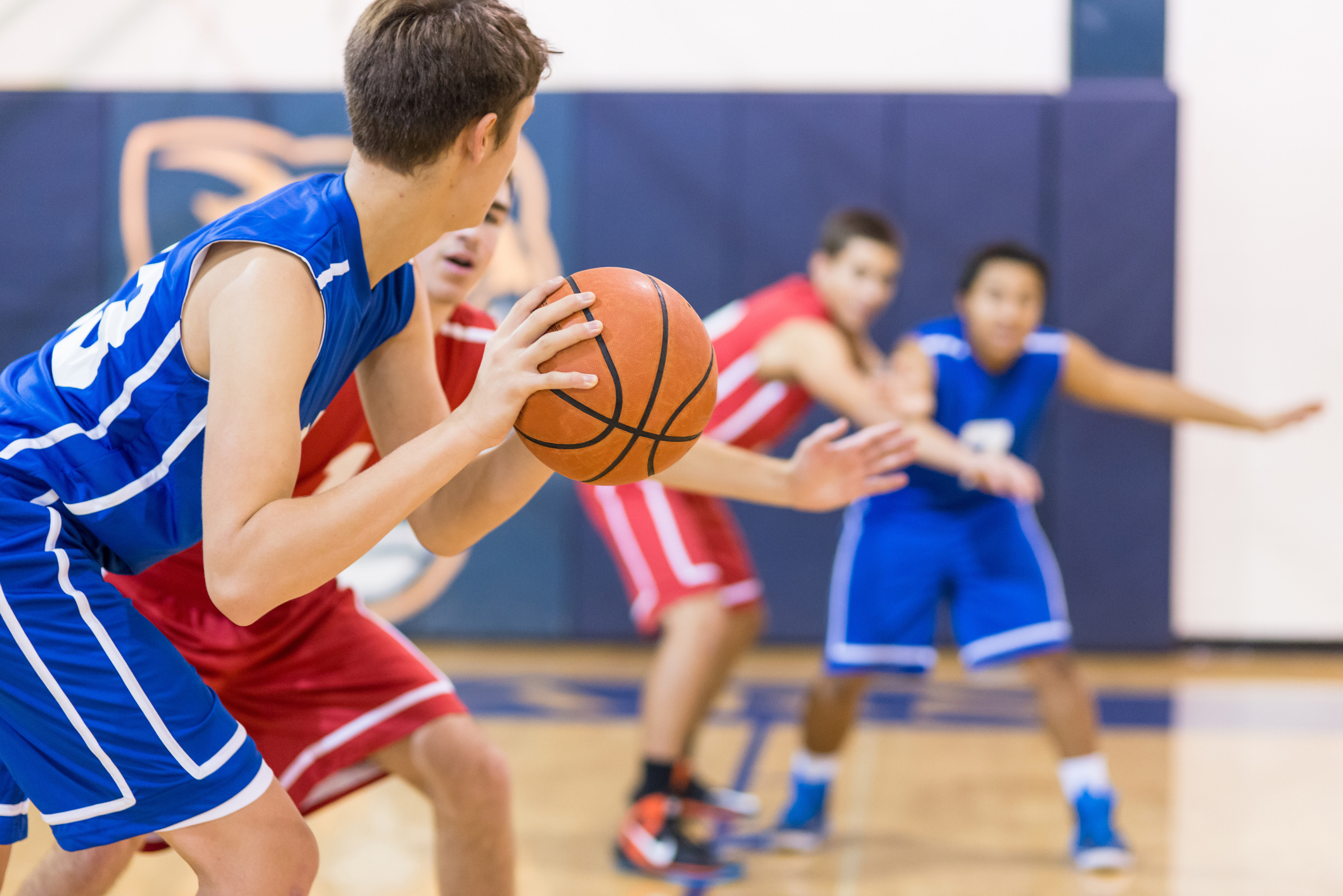 Basketball game action scene; two players in blue jerseys and two in red jerseys play intensely on the court