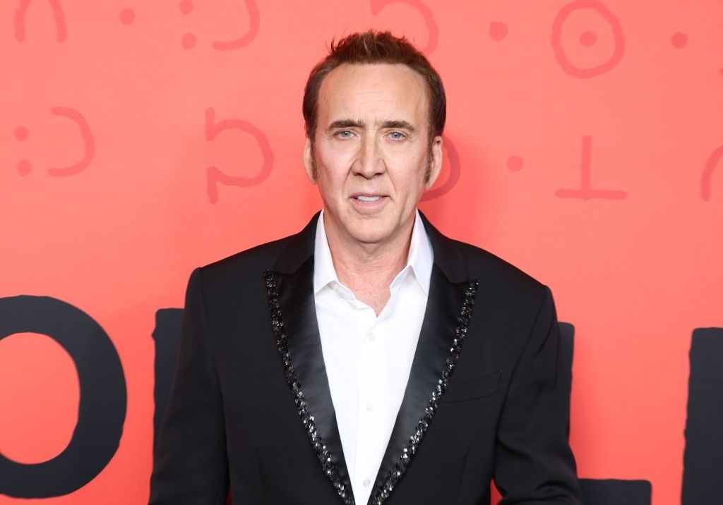 Nicolas Cage on the red carpet in a suit jacket with a sequined lapel detail, standing in front of a background with circular patterns