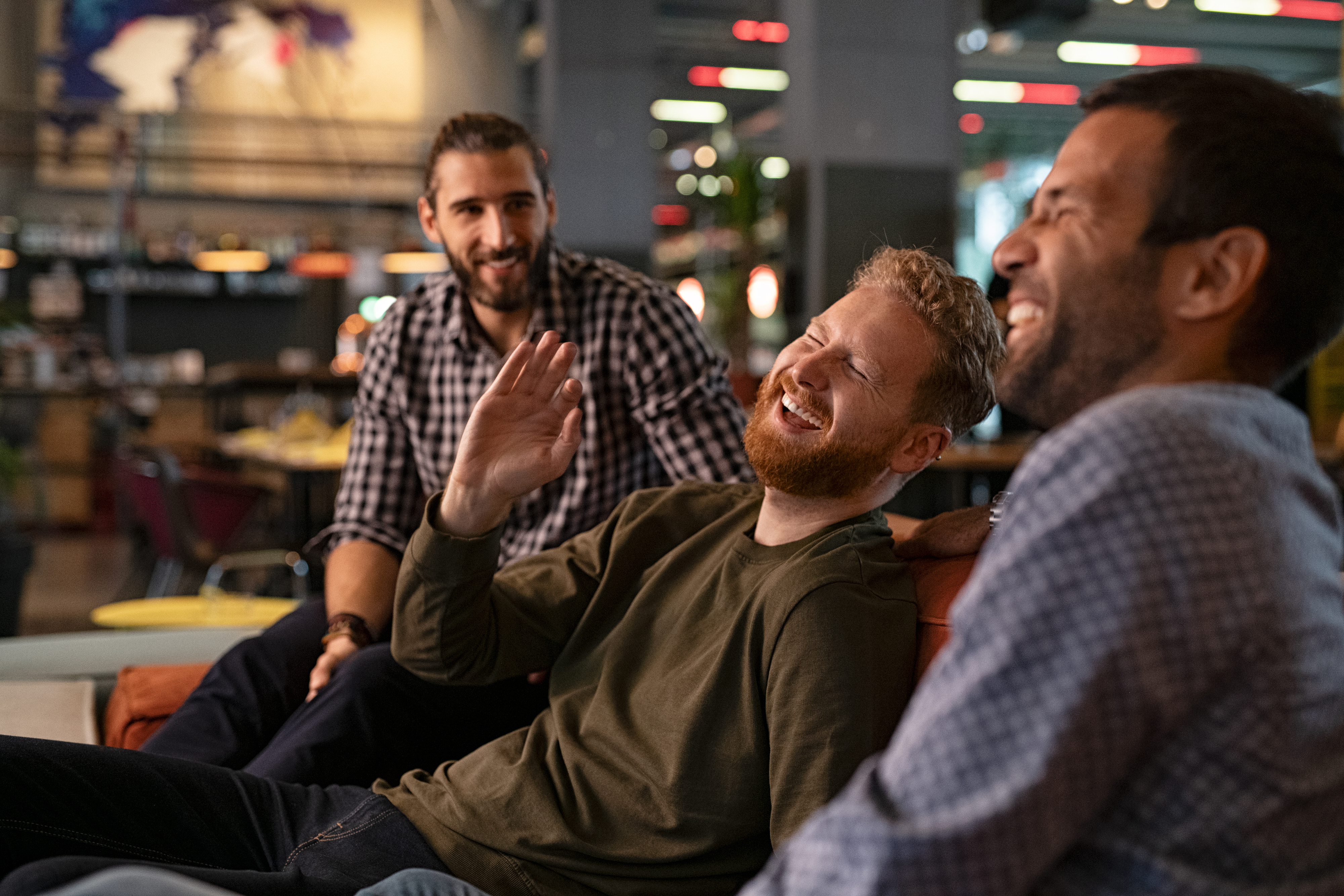 Three men are sitting and laughing together in a casual indoor setting