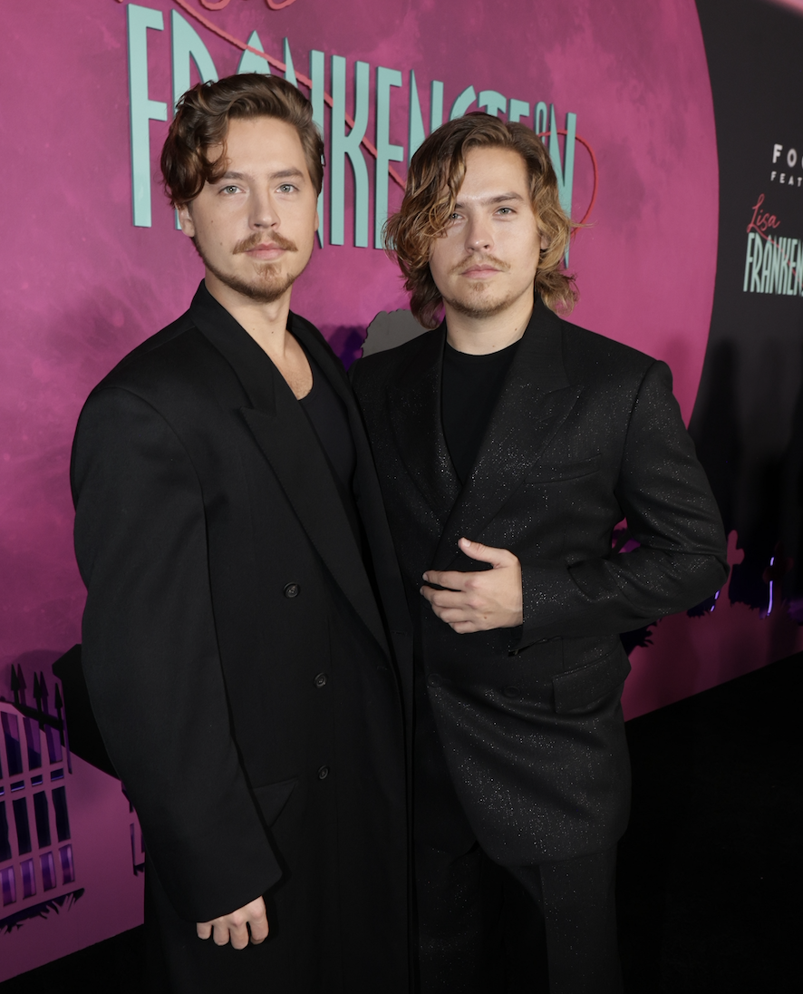 Dylan Sprouse and Cole Sprouse pose on the red carpet at a "Lisa Frankenstein" event, both wearing black suits