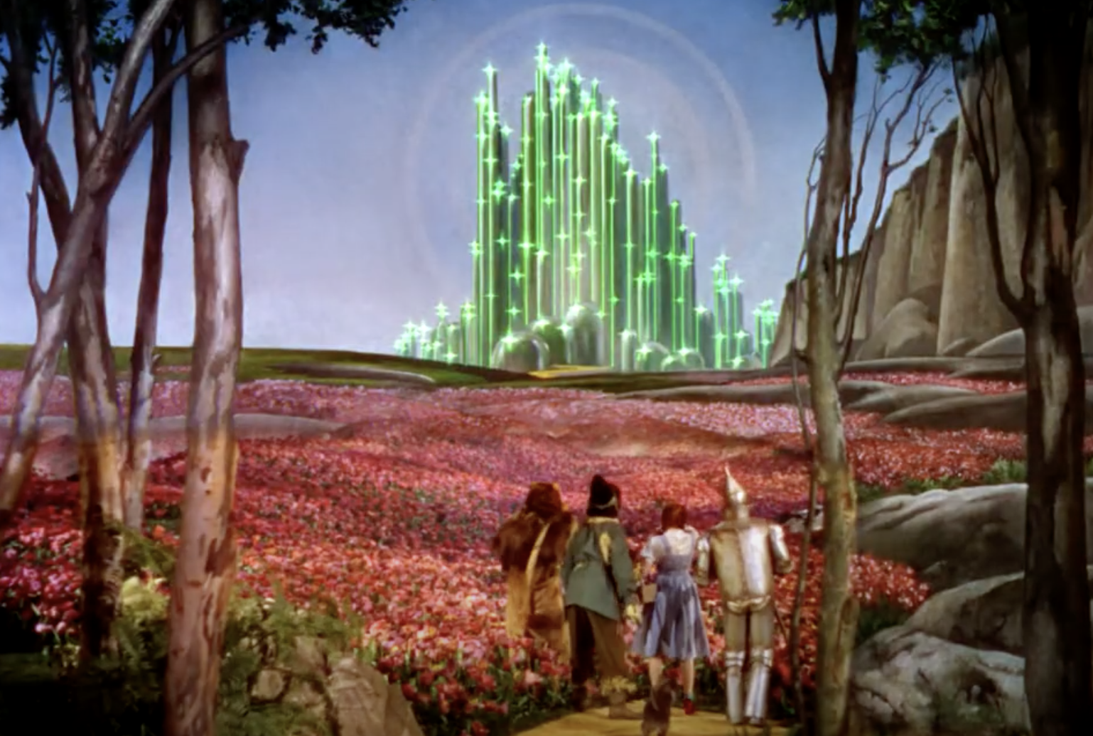 Dorothy, Toto, Scarecrow, Tin Man, and Cowardly Lion walk through a field of flowers towards the glowing Emerald City in "The Wizard of Oz."
