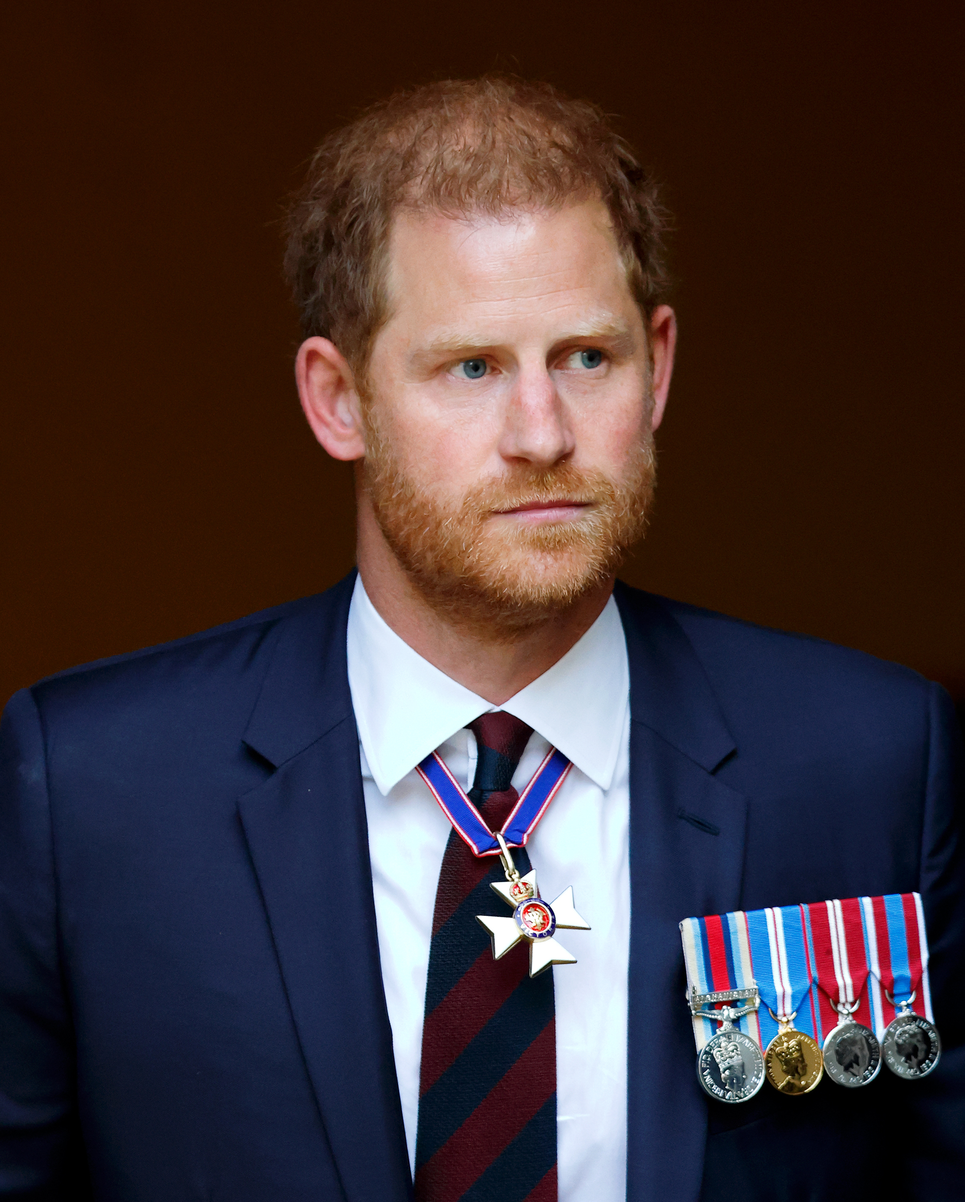 Prince Harry wearing a suit and tie adorned with various medals and a star-shaped pin during a formal event