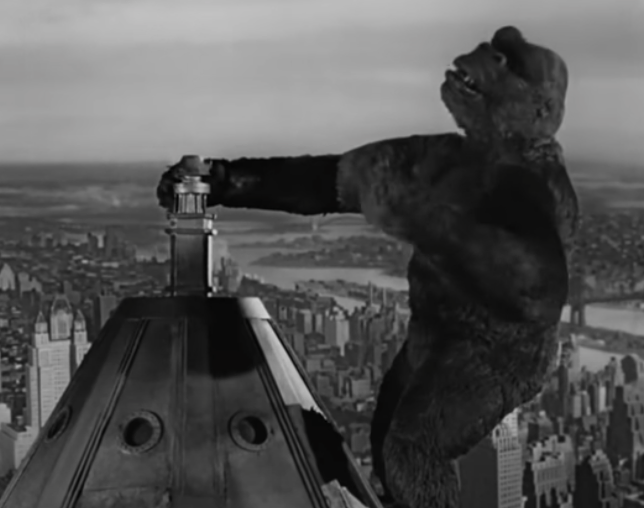 King Kong clinging to the Empire State Building, towering over the New York City skyline, in a famous scene from the classic film "King Kong."