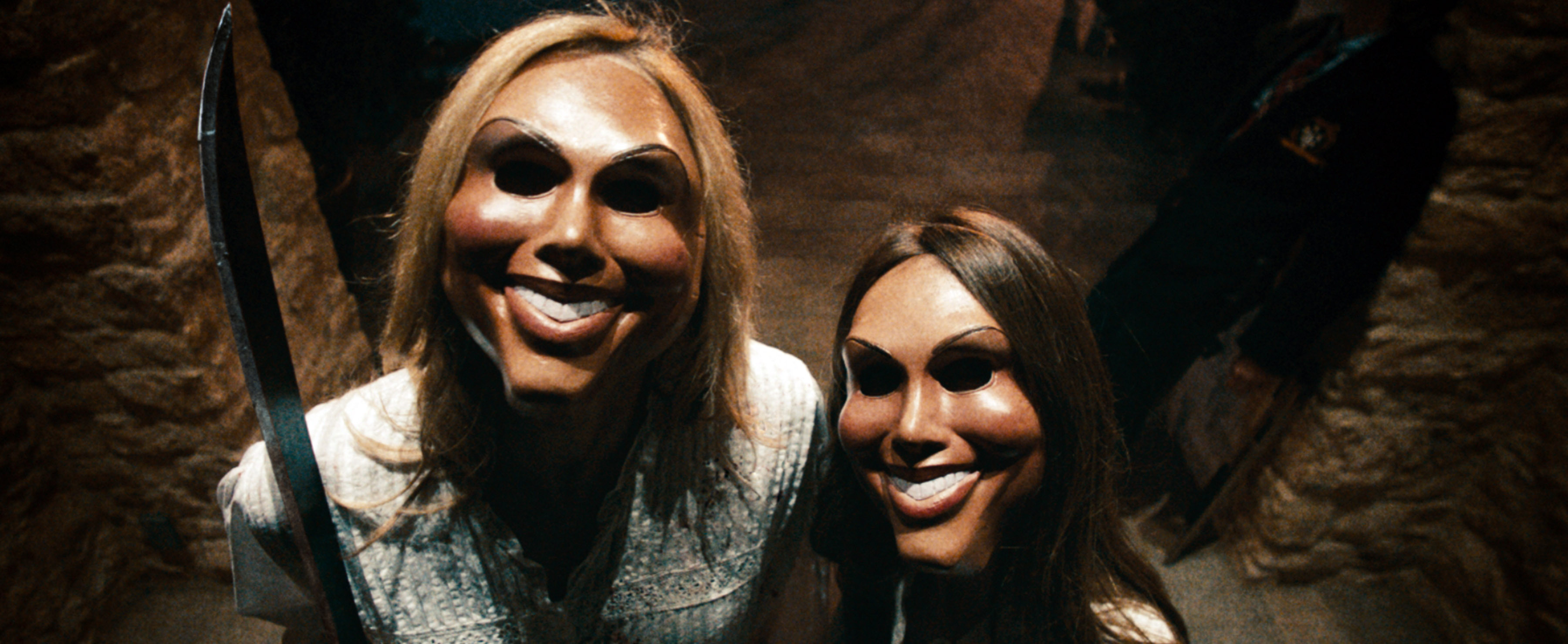 Two characters from &quot;The Purge&quot; wearing creepy smiling masks, standing outside a home at night