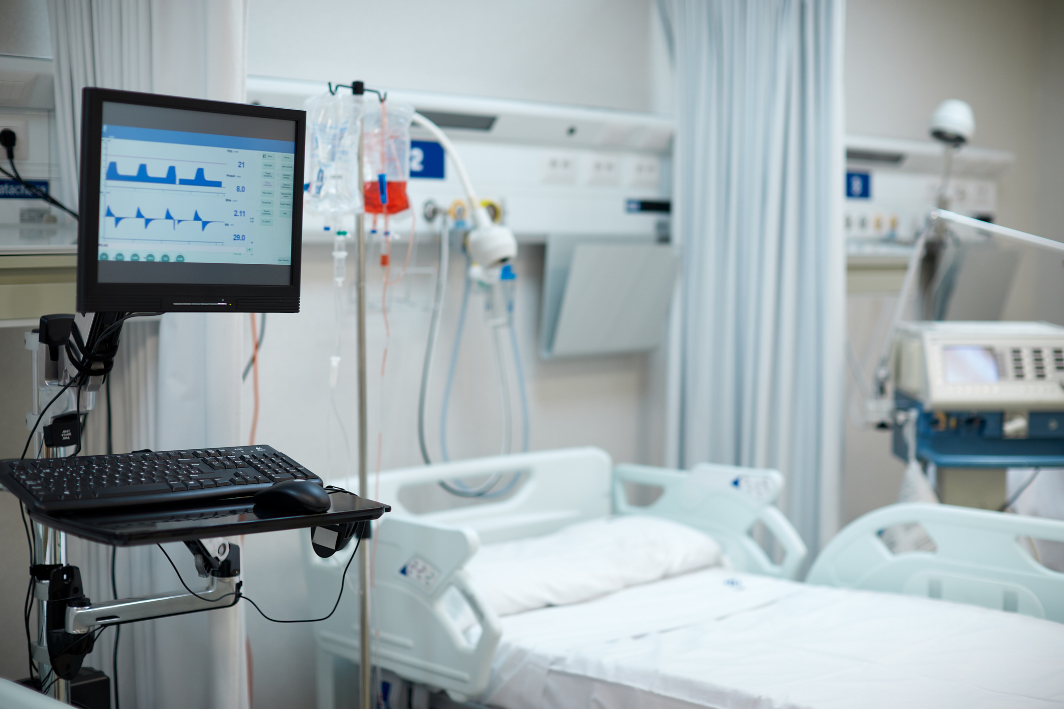 A hospital room with a monitor displaying patient vitals, an empty bed, IV and medical equipment